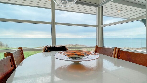 Een eettafel met een glazen schaal als middelpunt, grote ramen en uitzicht op zee.