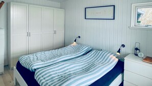 Een slaapkamer met een bed, nachtkastje, dressoir, kledingkast en een ingelijst schilderij aan de muur.