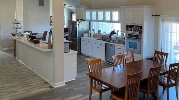 A spacious kitchen with white cabinets, a dining area with a wooden table and chairs, and a chandelier. - Stillhouse Lake Fishing Retreat -Cedar Creek Ranch, 10 Acres + Boat Parking (Salado)