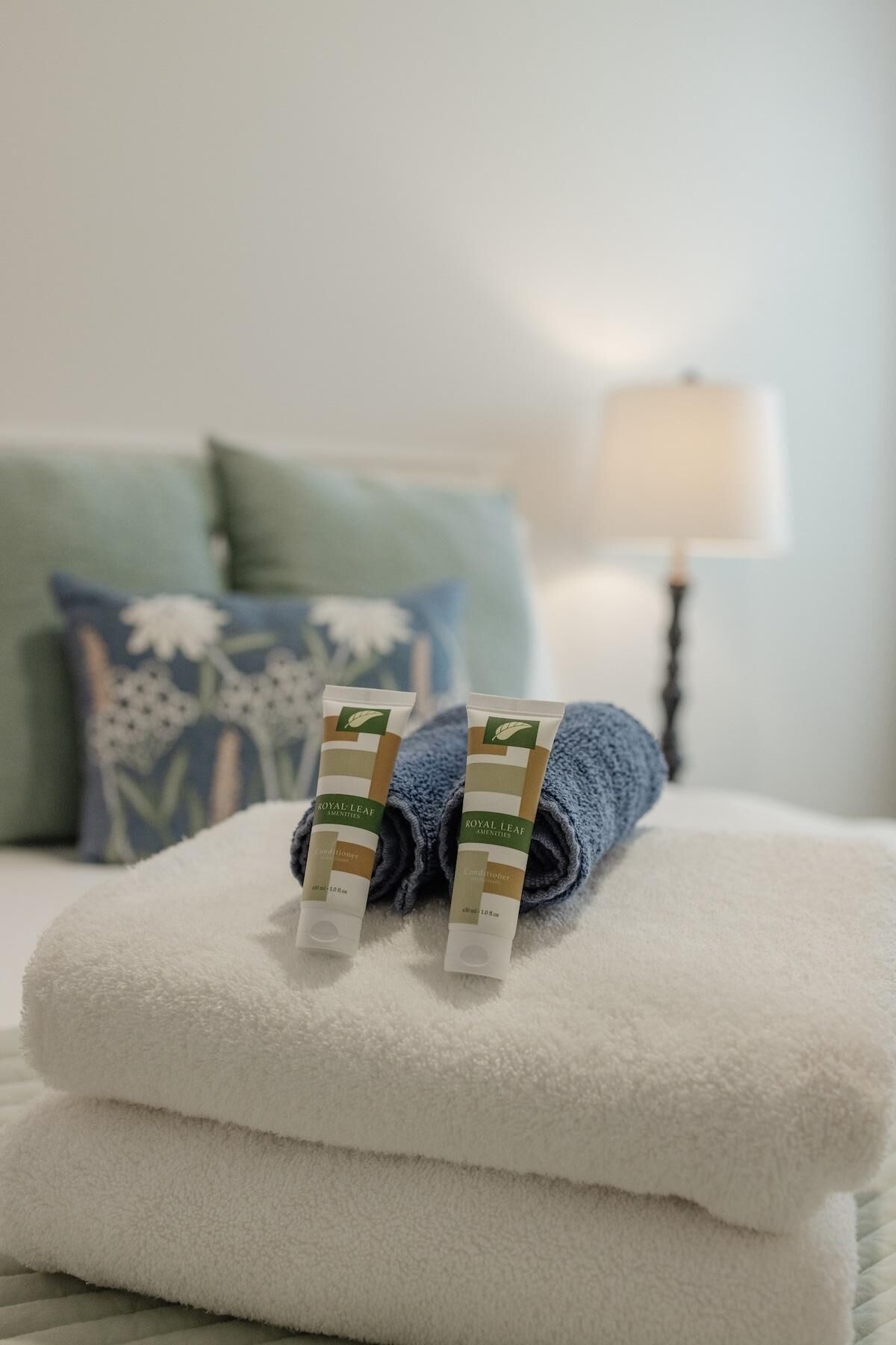 Een keurig opgevouwen witte handdoek met twee tubes Royal Leaf Amenities conditioner erboven.