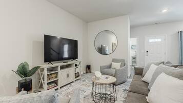 A modern living room with a flat-screen TV, a round mirror, and a grey sofa.