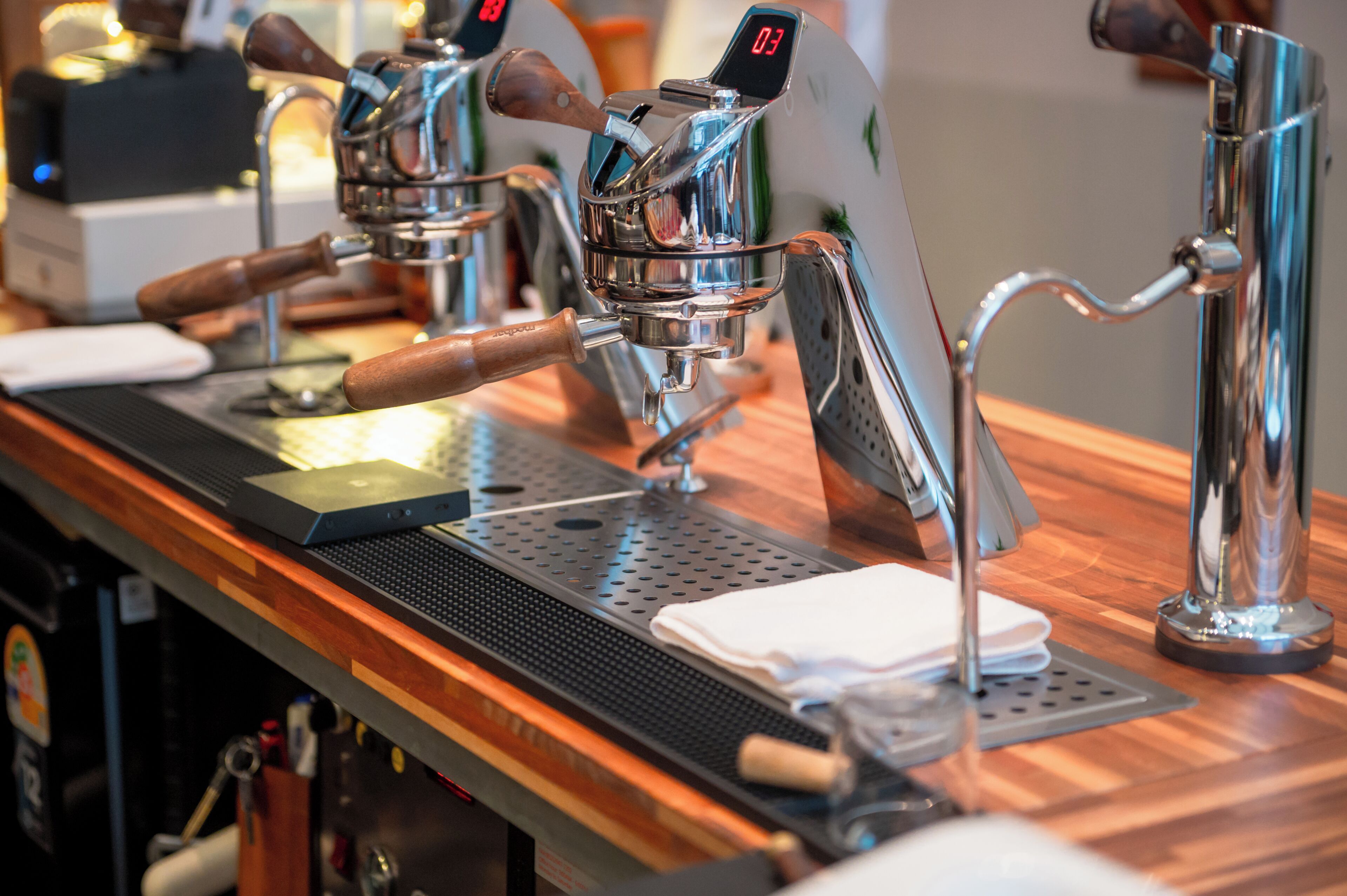 A coffee machine with a digital display, a wooden counter, and a metal drip tray.