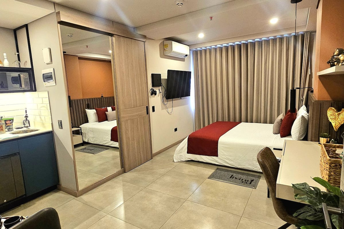 A hotel room with a bed, a desk, a mirror, a TV, and a minibar.