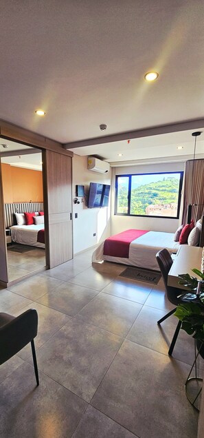 A modern hotel room with a large bed, a desk, a TV, and a view of a green landscape. - LINVING 35 8TH FLOOR VIP (Medellín)