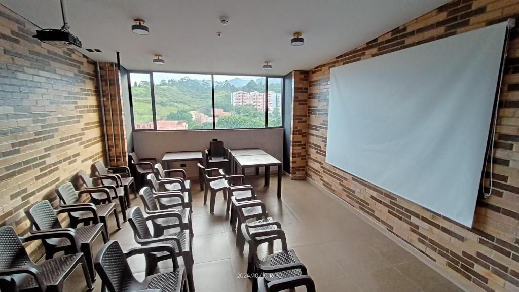 A conference room with a large projection screen, rows of chairs, and a view of buildings through large windows.