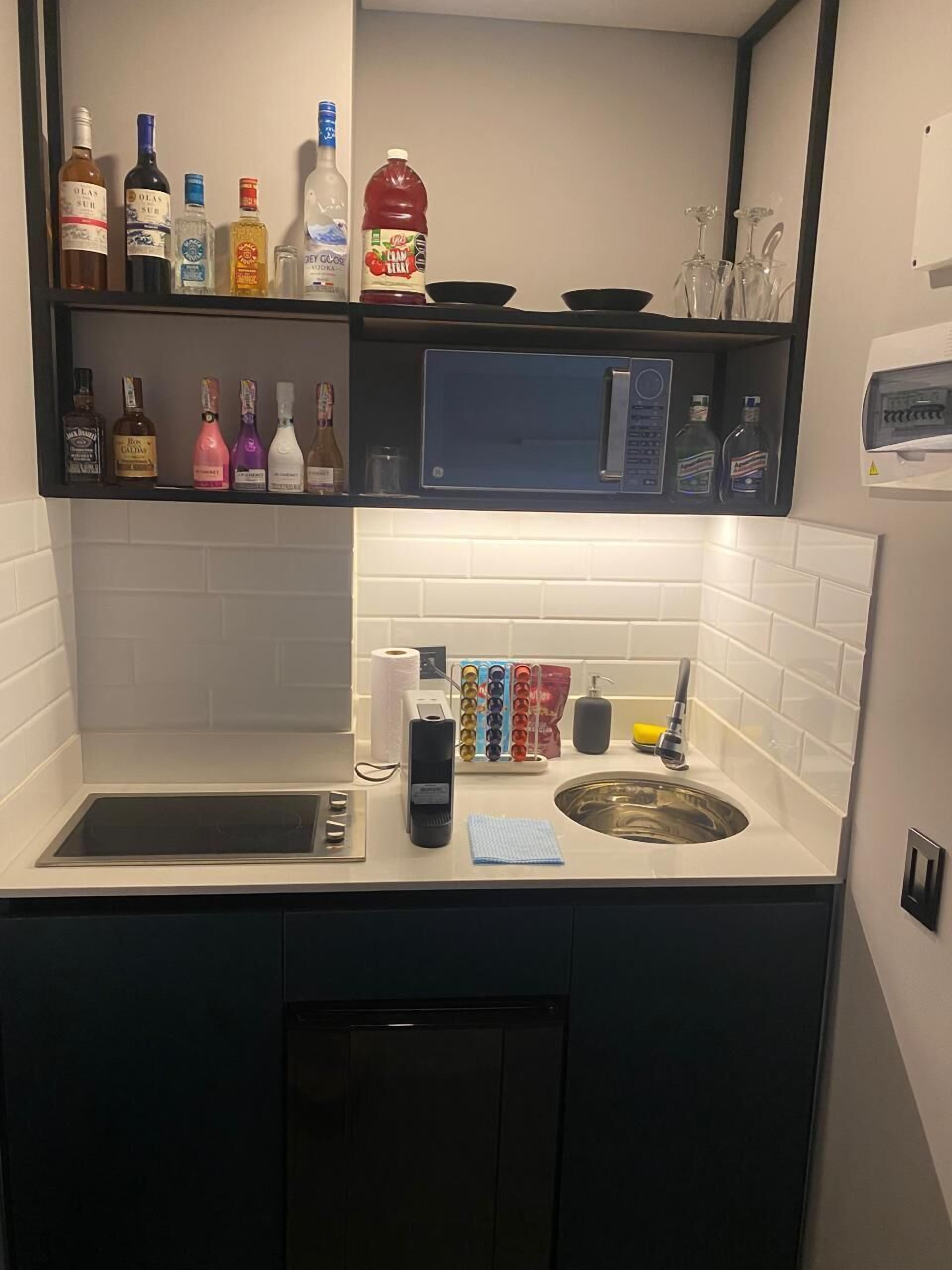 A compact kitchen with a microwave, sink, and various bottles on shelves.