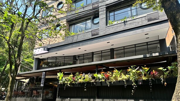 A modern building with a glass facade, multiple floors, and outdoor planters with various plants. - LINVING 35 8TH FLOOR VIP (Medellín)