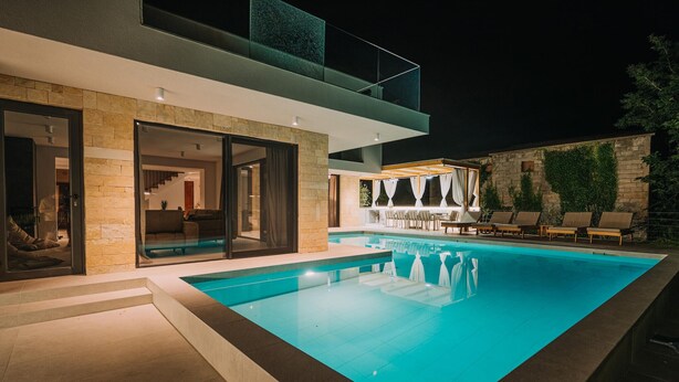 A modern outdoor pool area with a glass-enclosed lounge, stone walls, and a clear blue pool. - Beautiful home in Privlaka with sauna (Privlaka)