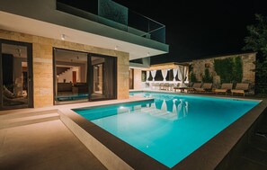 Uma área de piscina moderna ao ar livre, com um espaço de estar envidraçado, paredes de pedra e piscina azul cristalina.