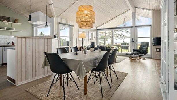 Uma sala de jantar ampla, com uma mesa grande, cadeiras pretas e uma luminária pendente trançada.