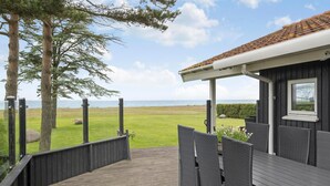 Um deck de madeira com móveis de vime, com vista para uma área gramada e o mar.