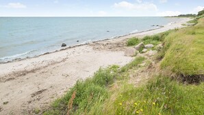 Uma praia com areal, algumas rochas e vegetação verde.