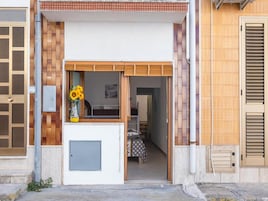 Una entrada moderna a un edificio con puerta de madera, un ventanal con un florero, y un pasillo interior visible.