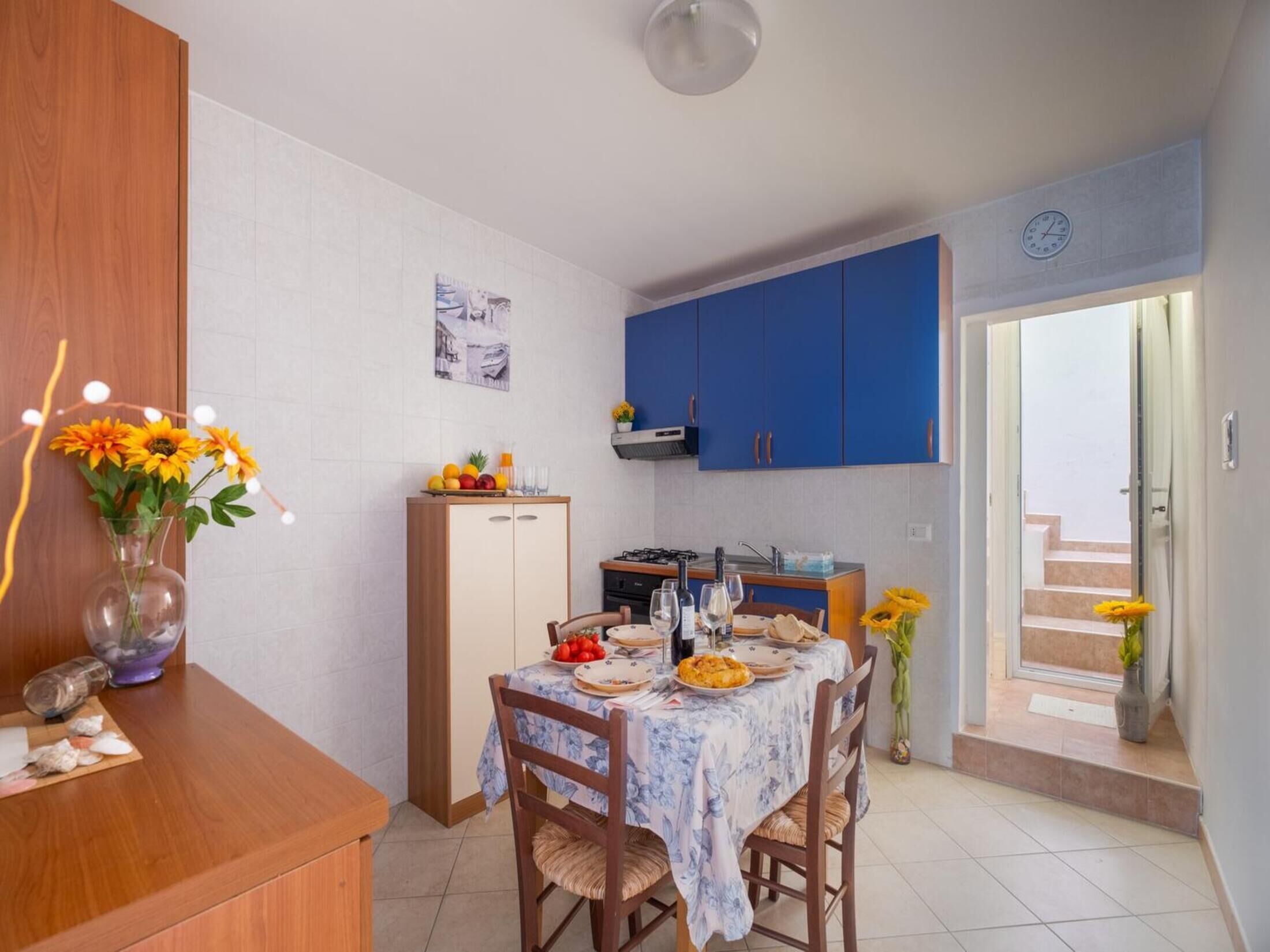 A compact kitchen with blue cabinets, a dining table set with plates and glasses, and a small refrigerator.