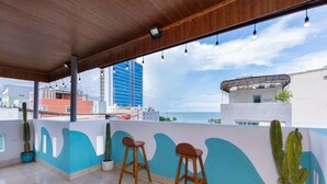 Terraço no telhado com dois banquinhos de madeira, cactos em vasos e vista para a cidade e o oceano.