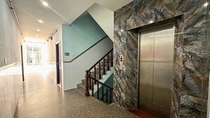 Um corredor com parede de mármore, um elevador e uma escada.