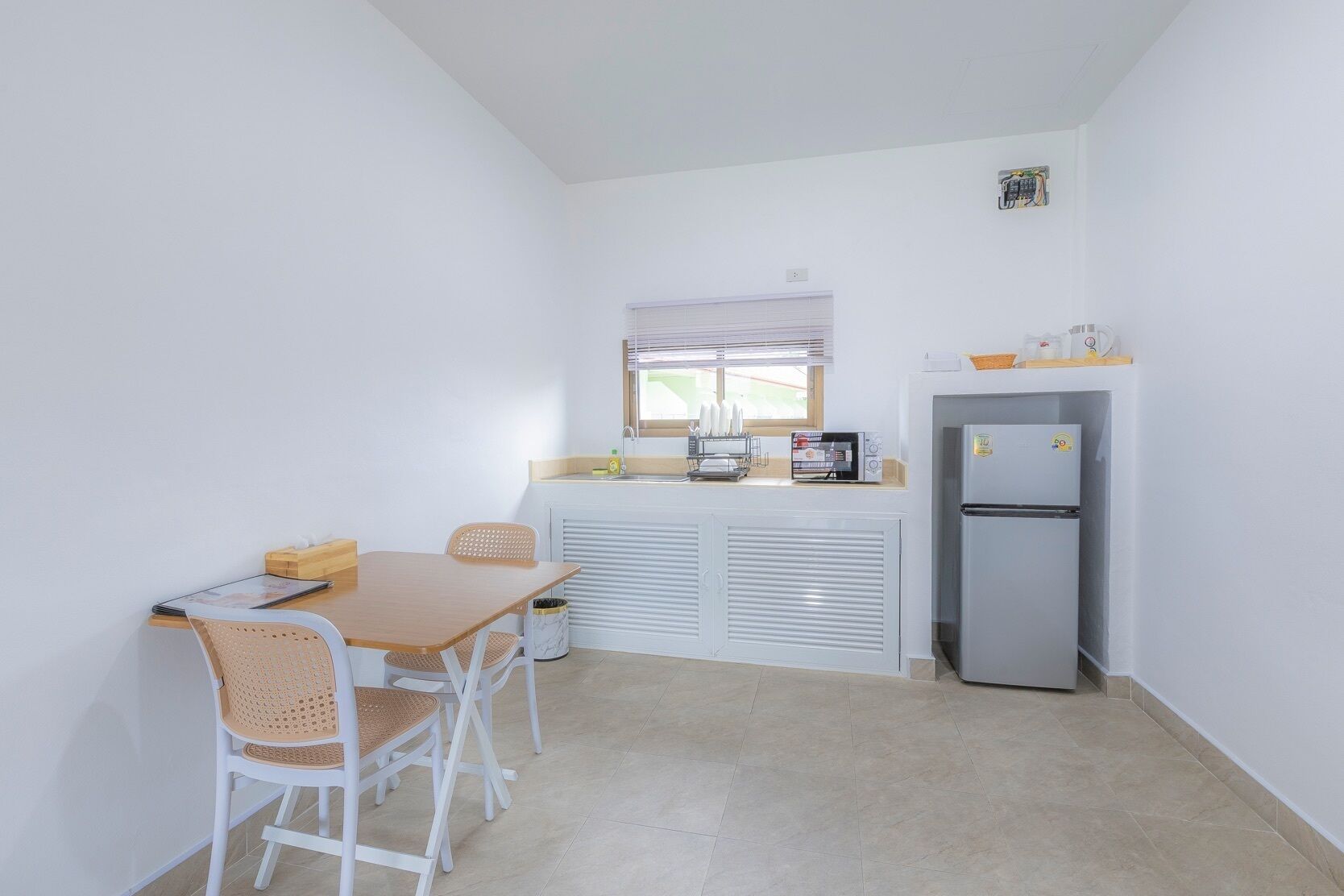 A compact kitchen with a dining table, chairs, a refrigerator, and a window with blinds.