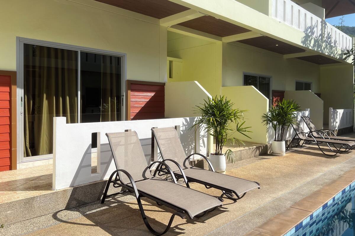 A poolside area with lounge chairs, a potted plant, and a staircase leading to a balcony.
