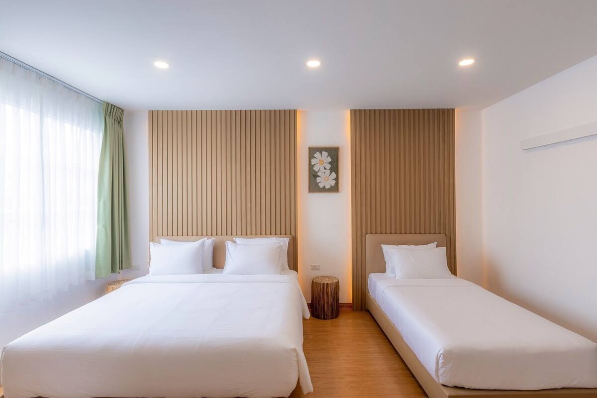 A hotel room with two beds, a wooden panel wall, a small round table, and a window with sheer curtains.