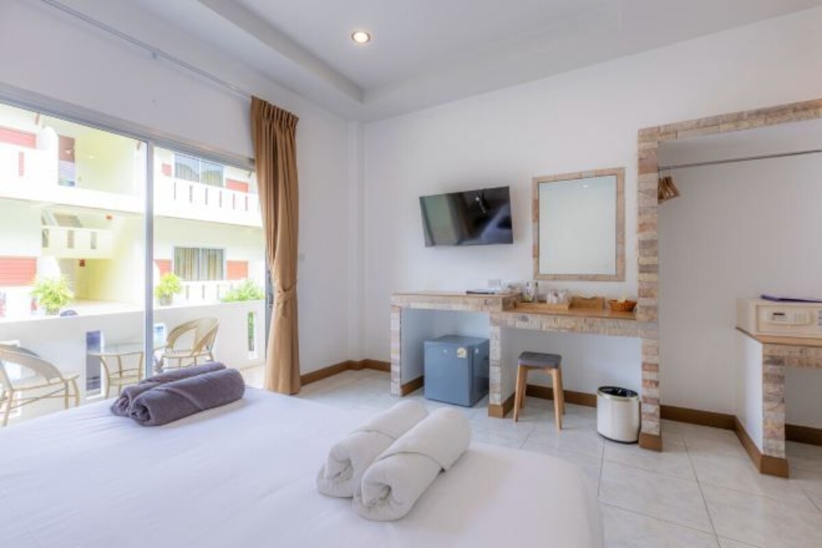A hotel room with a bed, a desk, a TV, and a balcony with chairs.