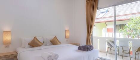 A hotel room with a large bed, two pillows, a nightstand, a wall-mounted lamp, and a view of the outside balcony.
