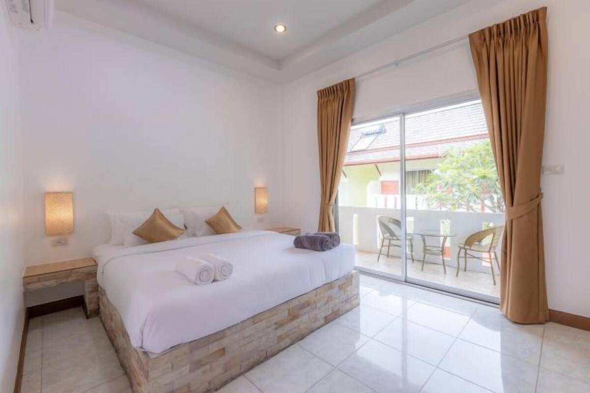 Un dormitorio con una cama grande, una mesita de noche, dos lámparas de pared, un ventanal corredero a un balcón y vistas al exterior.