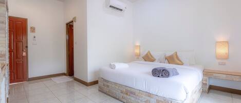 A hotel room with a bed, a nightstand, a wall-mounted air conditioner, and a door with a sign.