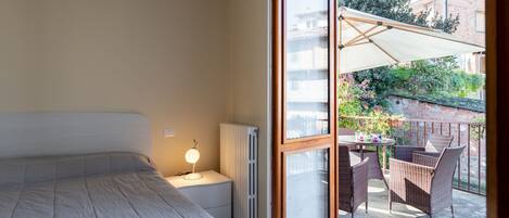 Un dormitorio con una cama grande, una lámpara de noche y vistas a un patio exterior con muebles de mimbre y una mesa.