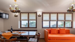 A dining area with a wooden table, chairs, and a sofa. There are windows with floral curtains and a television mounted on the wall. - Il Borghetto di Castagnole by Interhome (Castagnole Monferrato)