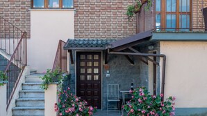A building entrance with a wooden door, a small covered porch, and two potted plants with pink flowers. - Il Borghetto di Castagnole by Interhome (Castagnole Monferrato)