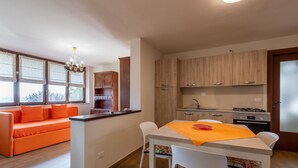 A modern kitchen with wooden cabinets, a dining table with chairs, and a bright window with curtains. - Il Borghetto di Castagnole by Interhome (Castagnole Monferrato)