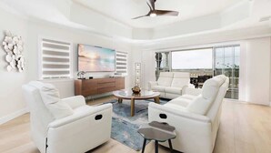 Un salon moderne avec des meubles blancs, un ventilateur de plafond et une grande fenêtre.