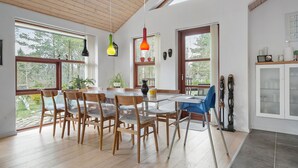 A dining area with wooden chairs and a table, large windows, and hanging pendant lights.