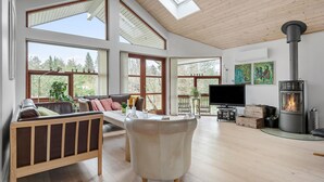 A spacious living room with a large fireplace, wooden flooring, and multiple windows offering views of the outdoors.