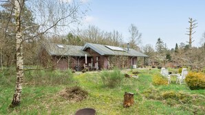 A rustic cabin with a sloped roof, surrounded by a natural landscape with trees and a grassy area.
