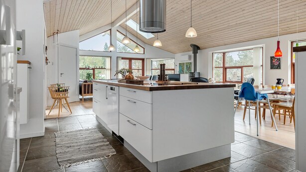 A spacious kitchen with a large island, wooden ceiling, and large windows.