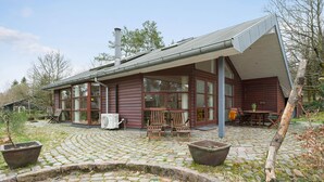 A rustic cabin with a stone patio, wooden furniture, and a large window overlooking the landscape.