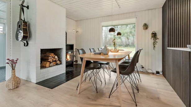 Ett modernt matområde med en öppen spis, en gitarr och utsikt över naturen.