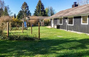 Une maison dotée d’une terrasse en bois, d’un espace de jeux avec des structures d’escalade et d’une pelouse bien entretenue.