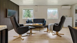 Ett rum med en mörkblå soffa, två svarta stolar, ett träbord och en tv som är monterad på väggen.