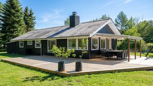 Ett modernt hus med en stor terrass, en inglasad uteplats och en skorsten.