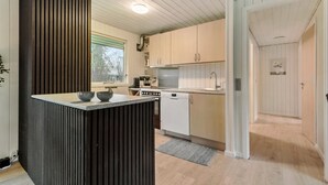 Ett modernt kök med en central köksö, vita skåp och ett fönster som släpper in naturligt ljus.