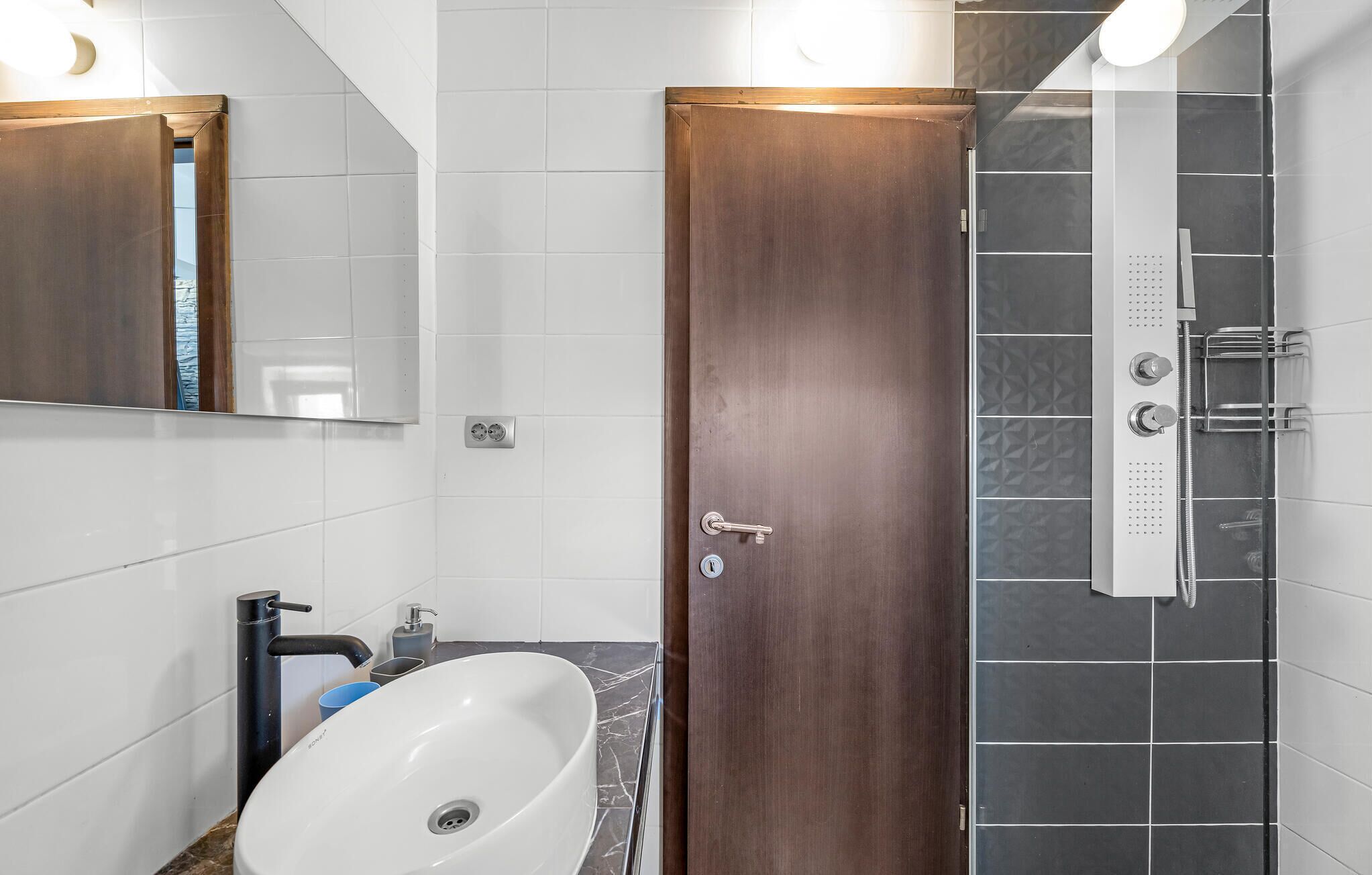 A modern bathroom with a white sink, a wooden door, and a shower area.