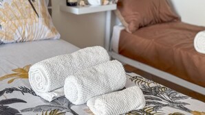Una cama bien hecha con un cubrecolcha marrón, una almohada blanca con diseño de plumas y una toalla blanca doblada sobre la cama.
