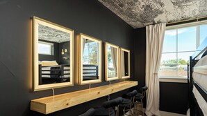 Ein Zimmer mit schwarzer Wand, drei gerahmten Spiegeln, einem Holzregal mit Barhocker und einem Fenster mit Vorhängen.