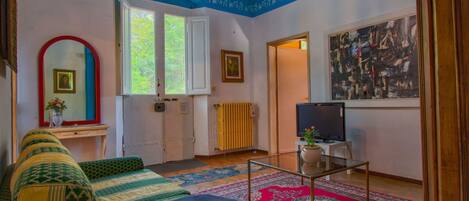 A room with a bed, a TV, a radiator, a window, and a painting on the wall.