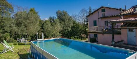A rectangular swimming pool with a white and blue border, surrounded by a grassy area with lounge chairs.