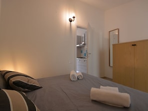 Een slaapkamer met een bed, kussens, een houten kledingkast en een zichtbare badkamer door een geopende deur.