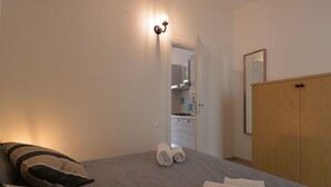 Quarto com cama, almofadas, um guarda-roupa de madeira e um banheiro visível por uma porta aberta.