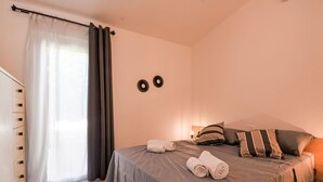 Quarto com cama, mesa de cabeceira, cômoda, janela com cortinas e decoração nas paredes.